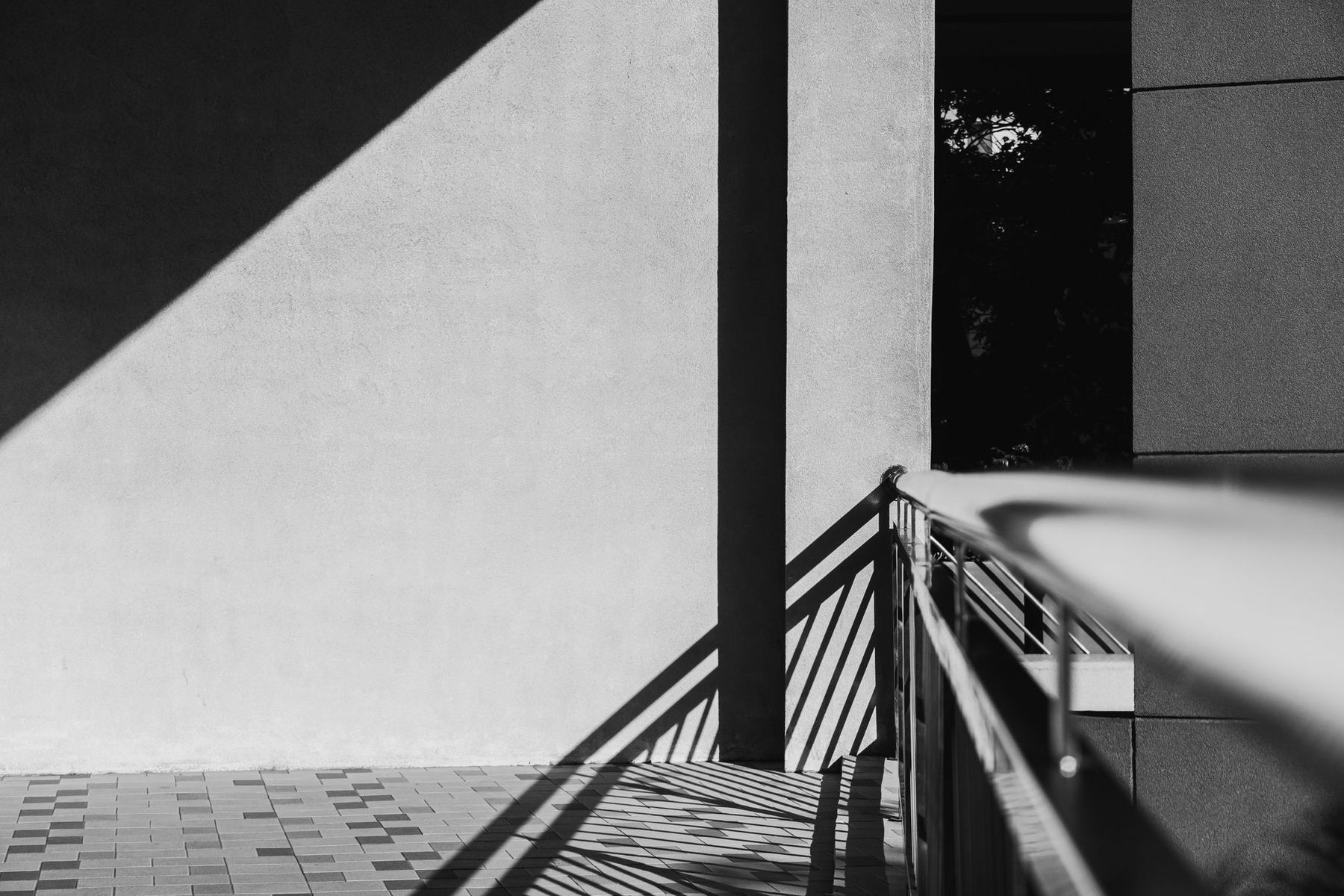 Light and shadow falling across a plain concrete wall and a stair rail