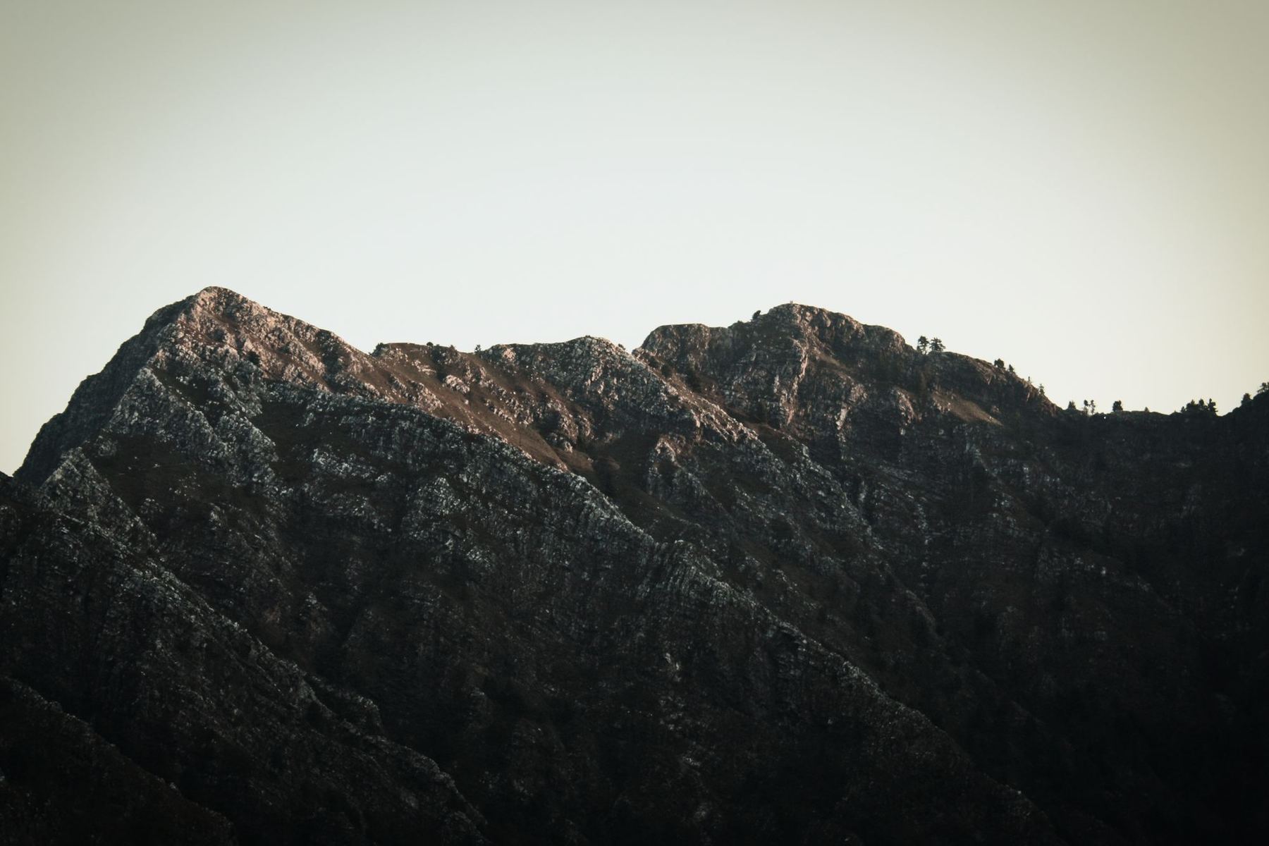 A dark mountain ridge under a pale sky