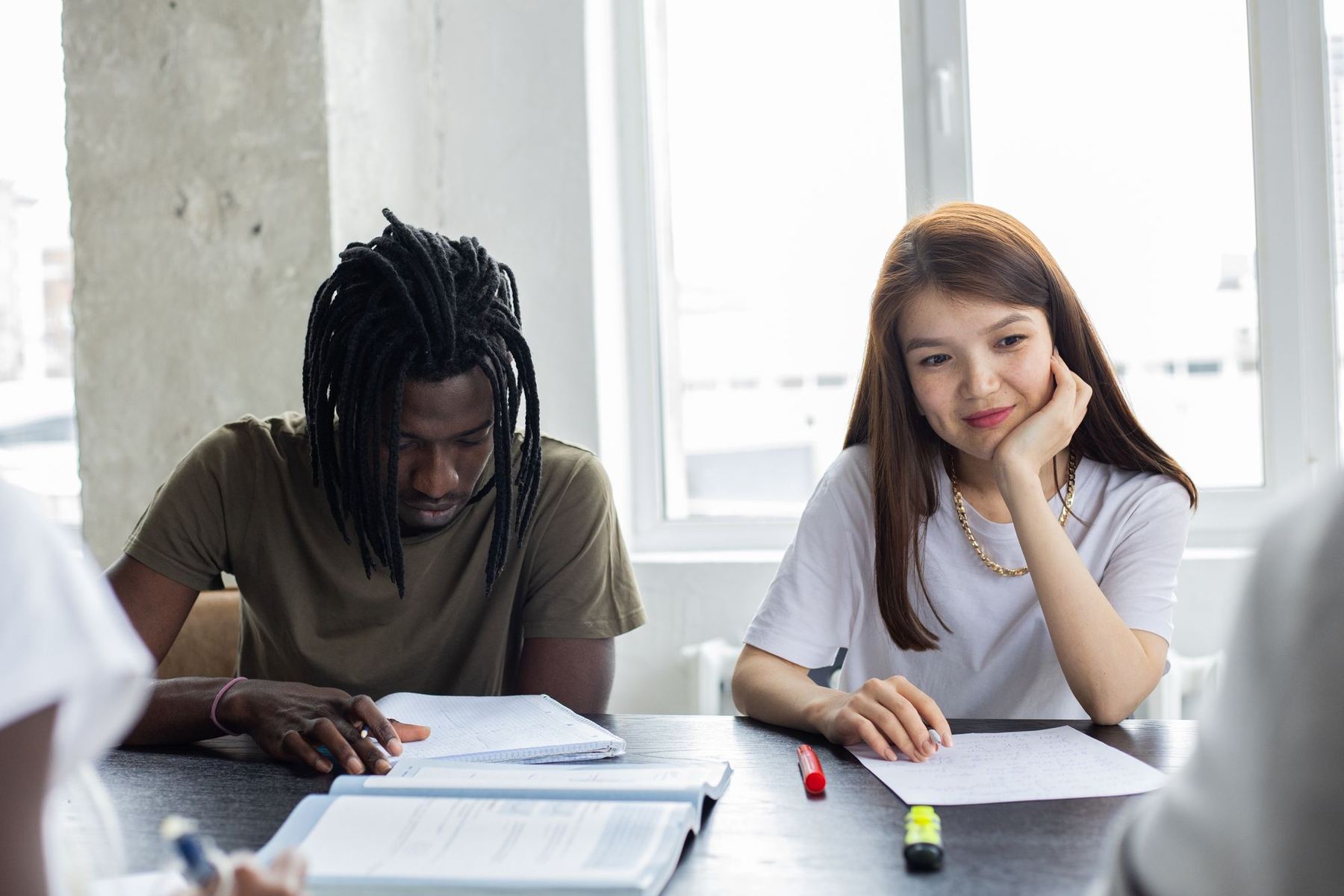 Two young people working side by side at a table in daylight